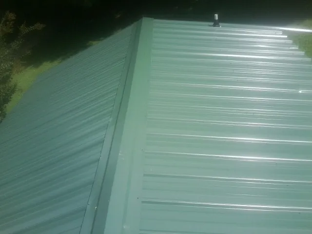 New green metal panels meeting at the ridge of a roof — Flat Roof Repair work by our crew in Cape Canaveral