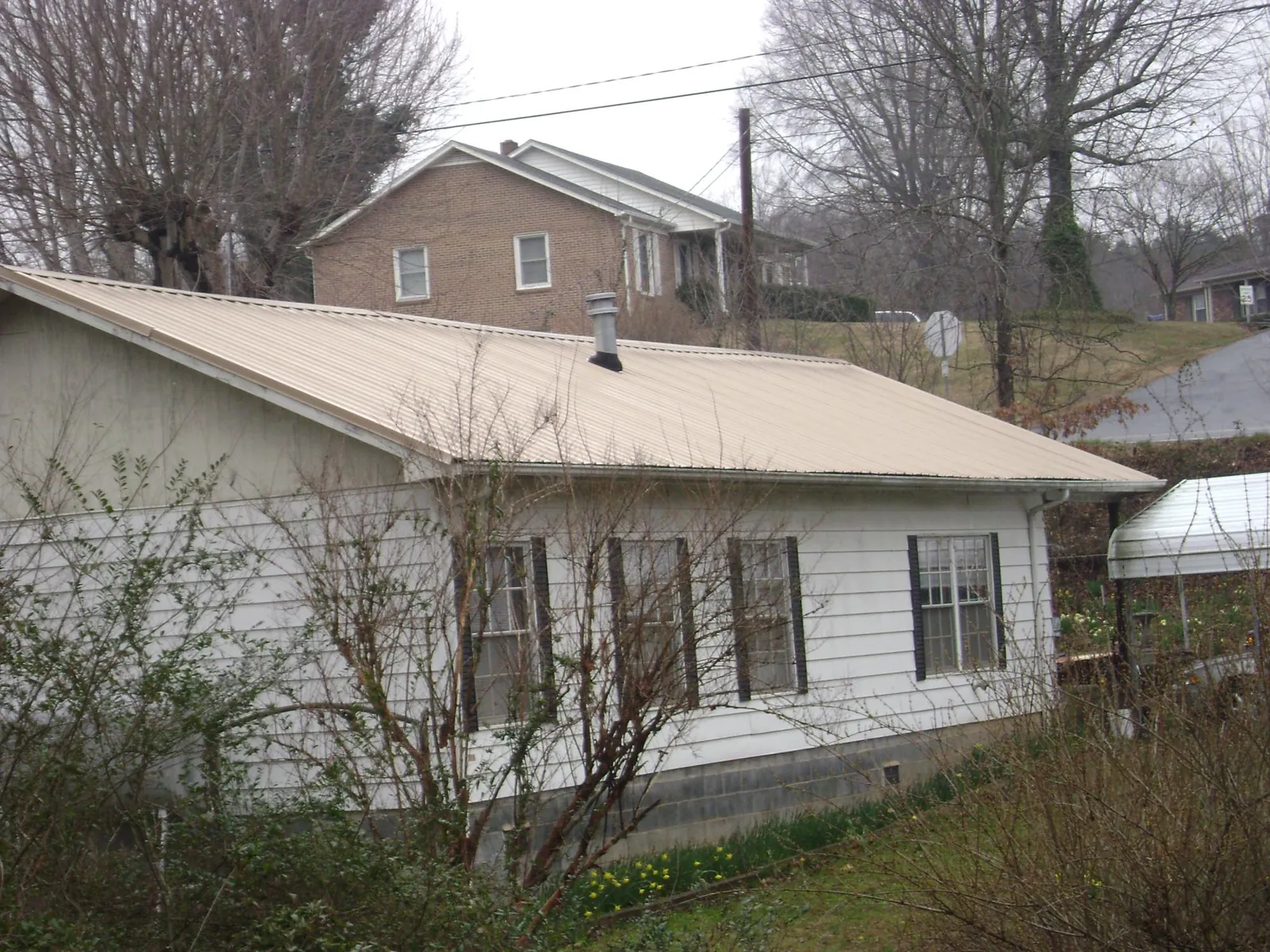 Tan metal roof on a white sided house set into a hillside — Commercial Roofing by Roofing Brothers in Cape Canaveral